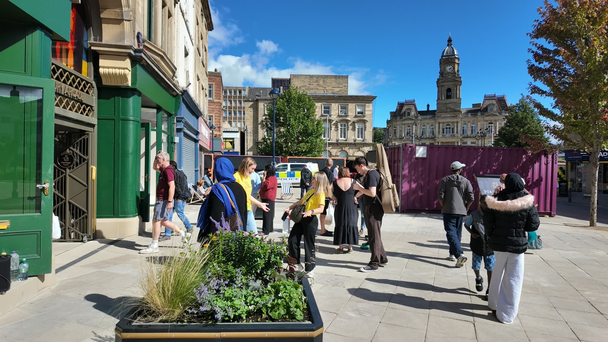 Dewsbury Market Place on a sunny day with people outside the cafés